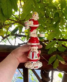 a hand holding a red and white santa clause ornament on top of a tree