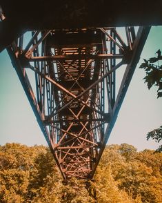 the underside of a tall metal bridge with trees in the foreground and blue sky above