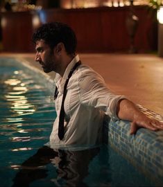 a man wearing a tie leaning on the edge of a swimming pool