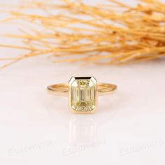 a yellow diamond ring sitting on top of a white table next to some dry grass