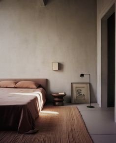 a bed in a room with a brown blanket on top of it and a lamp next to it