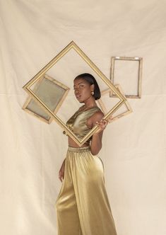 a woman standing in front of a white backdrop holding a gold framed object with her hands