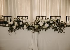 the table is set up with white flowers and greenery for an elegant wedding reception