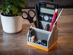 a pen, scissors, and other office supplies sit in a holder next to a potted plant