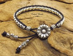 a black leather bracelet with silver beads and a flower on the clasp, sitting on top of a rock