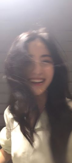 a woman with long dark hair smiling and holding her hands behind her back to the camera