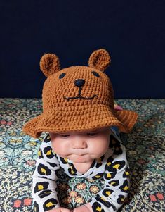 a baby wearing a crochet bear hat on top of a bed next to a blue wall