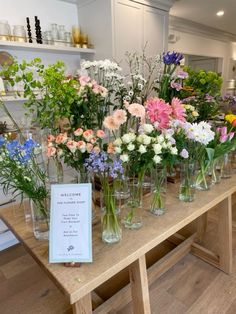 a wooden table topped with lots of vases filled with different types of flowers and greenery