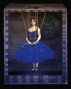 a woman in a blue dress and necklaces is suspended from a wooden frame with chains