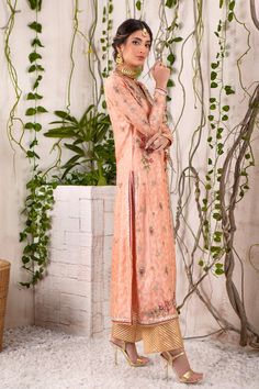 A captivating shade of peach over a canvas of jacquard silk net, this chogha features myriad of colorful resham work in beautiful floral embroidery, further enhanced with dabka, sequins, pearls, beads & crystals in rose gold, antique gold &silver tones on neckline, hem, sleeves & back. Beautifully Hand-crafted tassels for additional style element. A classy Raspberry & Gold Jacquard Chunri dupatta adds a beautiful pop of color and dhanak embellished tissue izaar elevates the festive look of this Resham Work, Designer Outfit, Shades Of Peach, Festive Look, Pakistani Designers, Floral Embroidery, Antique Gold, Crystal Beads, Custom Sizing