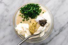 a glass bowl filled with yogurt, chives and seasoning next to a spoon