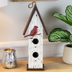 a bird house on a table next to a potted plant and a candle holder