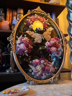 a mirror with flowers in it sitting on a table next to a lamp and bookshelf