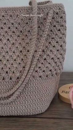 a crocheted purse sitting on top of a wooden table next to a pink flower