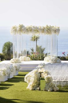 an outdoor ceremony setup with white flowers and candles on the grass, overlooking the ocean