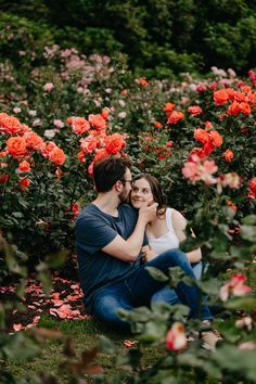 a man and woman are sitting in the middle of some red flowers with their arms around each other