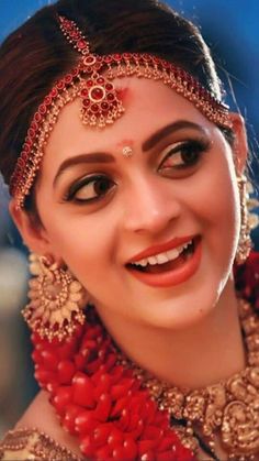 a woman wearing a red and gold head piece with jewelry on her face, smiling at the camera