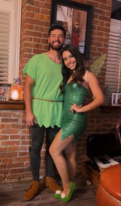 a man standing next to a woman in a green dress near a brick wall and window