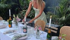 a woman is setting the table with flowers and wine bottles on it for an outdoor dinner party