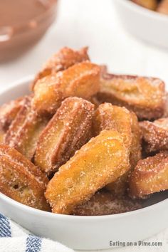 a bowl filled with sugared donuts on top of a white tablecloth next to bowls of dipping sauce