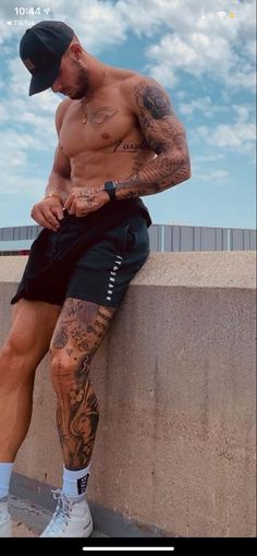 a man with tattoos sitting on a ledge looking at his cell phone while wearing shorts