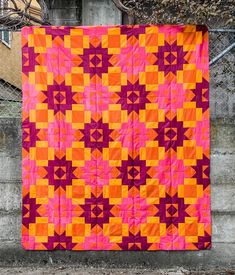 an orange and pink quilt hanging on a wall