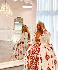 two women in white and red dresses are looking at their own reflection in the mirror