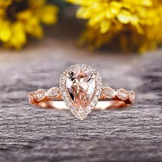 an engagement ring with a pear shaped morganite surrounded by small diamonds on a wooden surface