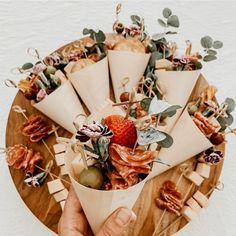 a hand holding a paper cone filled with fruit and veggies on a wooden platter