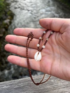 a person is holding out their hand with some beads on it and water in the background