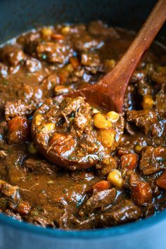 a wooden spoon in a pot filled with stew and beans, ready to be eaten