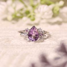 a close up of a ring with a purple stone in the middle and white flowers behind it