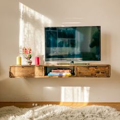 a flat screen tv sitting on top of a wooden shelf next to a white rug