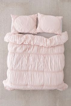 a pink comforter and pillows on a bed in a room with concrete flooring