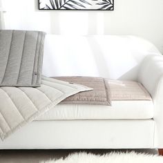 a white couch sitting next to a window with a blanket on it's back