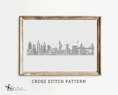 the cross stitch pattern is displayed in a wooden frame, with an image of a city skyline