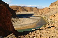 there is a river in the middle of some rocks and sand, with mountains in the background