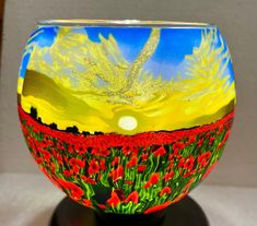 an artistic glass vase with red flowers painted on the outside and yellow sky in the background