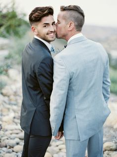 two men in suits standing next to each other and smiling at the camera with their faces close together