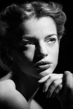 a black and white photo of a woman with her hand on her chin looking at the camera