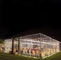 a large tent covered in lots of lights on top of a lush green field at night