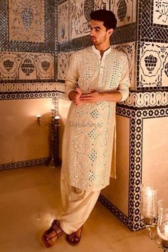 a man standing in front of a wall with decorative tiles and candles on the floor