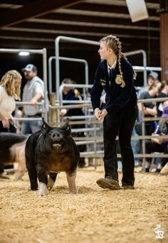 a woman standing next to a pig in a pen