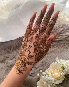 a woman's hand with henna on it and flowers in the foreground