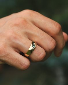 a man's hand wearing a gold ring with a diamond in the middle,