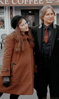 two people standing next to each other in front of a coffee shop on the street