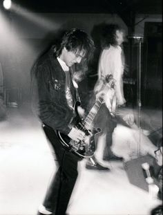 black and white photograph of man playing guitar in front of two other men on stage