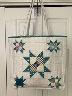 a white bag hanging from a hook on a door with blue and pink quilted stars