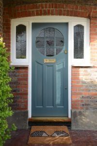 a blue front door on a brick house with two windows and a mat in front