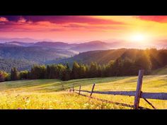 the sun is setting over a mountain range with a wooden fence in the foreground